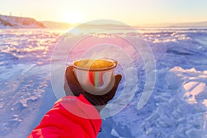 Tourist`s hand holding a steaming mug or cup with hot tea or coffee in winter landscape outdoors. Winter and rourism concept
