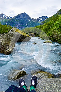 Tourist`s  legs above the river which is located near path to the Briksdalsbreen Briksdal glacier. Norway