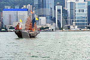 Tourist sailboat crosses Victoria harbor from Kowloon side to the Hong Kong Island. Scenic view of traditional Chinese wooden sail