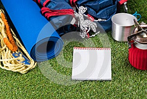 Tourist set on a green lawn for a hike in an expedition, with utensils for cooking food outdoors, with a place for writing, on a w