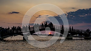 Tourist silhouettes stand on the bridge and gaze at the sunset