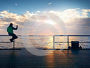 Tourist sit on mole handrail and takes pictures. Man enjoy morning at sea.