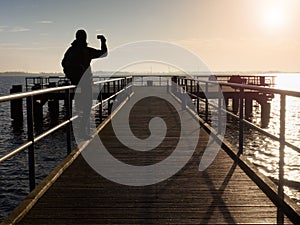 Tourist sit on mole handrail and takes pictures.Wooden boardwalk