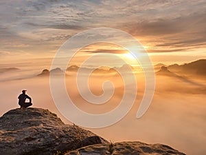 Tourist sit on peak of sandstone rock and watching into colorful mist and fog in morning valley. Sad man