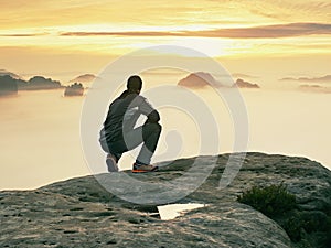 Tourist sit on peak of sandstone rock and watching into colorful mist and fog in morning valley. Sad man