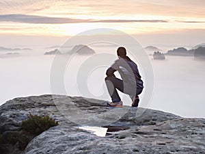 Tourist sit on peak of sandstone rock and watching into colorful mist and fog in morning valley. Sad man