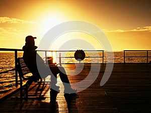 Tourist sit on wharf bench and enjoy misty sunny morning at sea. Smooth water