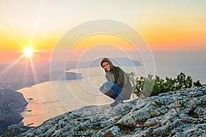 A tourist sits on a cliff overlooking the sea , watching the sun rise, travel concept