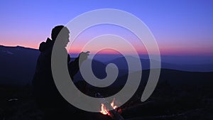 A tourist sits at night by a campfire in the mountains and writes messages on his smartphone. Tourist camp in the mountains