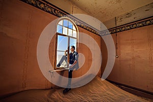 Tourist sits in the window of a room in the ghost town Kolmanskop, Namibia