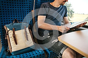 A tourist sits by the window in a train or commuter train and looks at a map