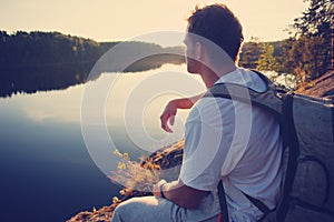 Tourist sitting on the cliff above the lake and looking far away at sunset