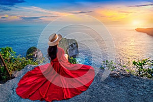 Tourist sitting on cliff and looking at sunset at Kelingking Beach in Nusa penida island, Bali, Indonesia