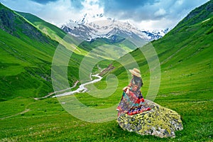 Tourist sitting on the rock at green pasture against highest georgian mountain Shkhara near Ushguli in Georgia