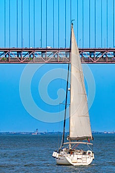 Tourist sleeping on top of a sailboat navigating the Tagus River with the red steel suspension bridge 25 de Abril above with