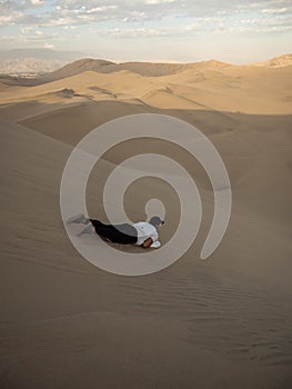 Tourist sliding down slopes of Huacahina sand dunes sandboarding adventure adrenaline fun extreme sports Ica Peru photo