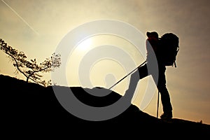 Tourist with sporty backpack and poles in hands stand on rock watching up to hill for next step.