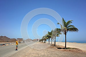 Tourist standing on road and taking photo of palm trees and sandy beach