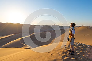 Tourist standing on sand dunes and looking at view in Sossusvlei, Namib desert, travel destination in Namibia, Africa. Concept of