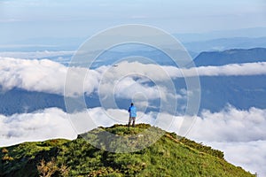 Tourist stays on the hill. Foggy summer morning. Landscape of high mountains and forests. The sun rays are shining through the fog