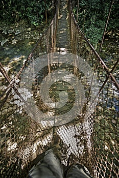 Tourist stepping on a suspension bridge across Rio Colorado in Rincon dela Vieja Volcano national park photo