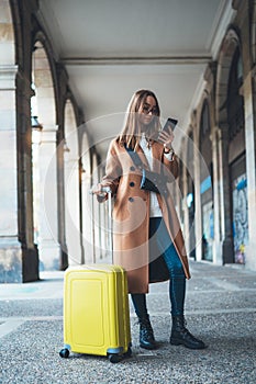 Tourist with suitcase holding smart mobile online phone. Girl travels in Barcelona. Holiday concept in Spain street. Traveler