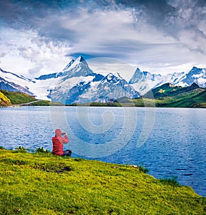 Tourist takes photo on mobile phone. Dramatic summer view of the Bachalpsee lake with Schreckhorn peak on background. Picturesque