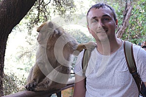 A tourist takes a selfie photo with a barbary macaque living in forest near the Ouzoud Falls.