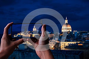 Tourist taking photo of illuminated at night Valletta old town and harbor in Valletta, Malta