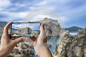 Tourist taking photo of stunning view of Dubrovnik city wall. Man holding phone and taking picture of fortress walls, rocky coast