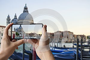 Tourist taking photo of traditional gondolas on famous Grande Canal with historic Basilica di Santa Maria della Salute in the