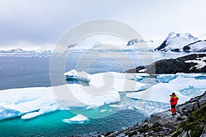 Tourist taking photos of amazing frozen landscape in Antarctica with icebergs, snow, mountains and glaciers, beautiful nature in