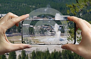 Tourist taking a picture of the erupting geyser old faithful at the Yellowstone national park, USA