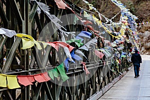 Tourist with tear colorful Tibetan prayer flags waving and swaddled with bridge over frozen river at Thangu and Chopta valley.
