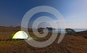 Tourist tent on a promontory near the sea on the background of the night sky