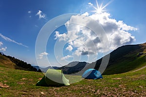 Tourist tents in camp among meadow in the mountain. Summer season, sunny day. The Alps, Italy, Europe.