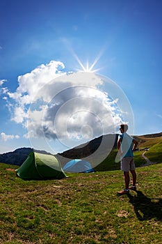 Tourist tents in camp among meadow in the mountain. Summer season, sunny day. The Alps, Italy, Europe.