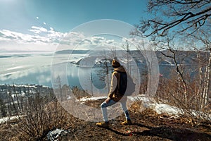 Tourist traveler with backpack stands on a mountain and looks at the beautiful view of lake Baikal. Winter landscape