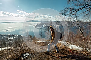 Tourist traveler with backpack stands on a mountain and looks at the beautiful view of lake Baikal. Winter landscape