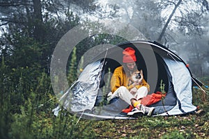 Tourist traveler in camp tent hugging red shiba inu on background froggy forest, hiker person with puppy dog in mist nature trip