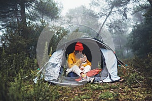 Tourist traveler in camp tent hugging red shiba inu on background froggy rain forest, hiker woman kiss puppy dog in mist nature