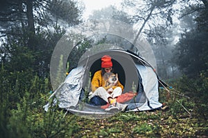 Tourist traveler in camp tent hugging red shiba inu on background froggy rain forest, smile woman with puppy dog in mist nature