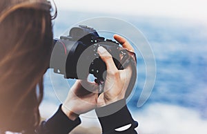 Tourist traveler photographer girl taking pictures of seascape on modern photo camera on background blue ocean view mockup sun