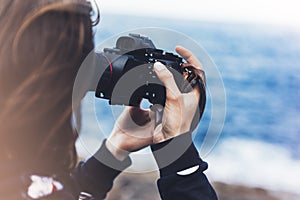 Tourist traveler photographer girl taking pictures of seascape on modern photo camera on background blue ocean view mockup sun