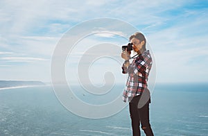 Tourist traveler photographer making pictures sea scape on photo camera on background ocean, hipster girl looking on nature horizo