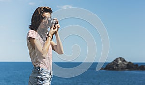 Tourist traveler photographer making pictures sea scape on vintage photo camera on background yacht and boat piar, hipster girl