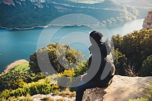 Tourist traveler sits on top mountain and enjoys river, hiker relax looking on blue sky clouds, background nature panoramic landsc