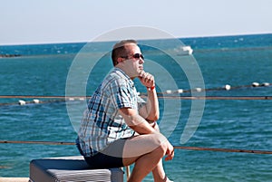 Tourist and traveler is sitting on his traveled suitcase on beach of hotel resort, enjoys view sea environment, nature landscape.