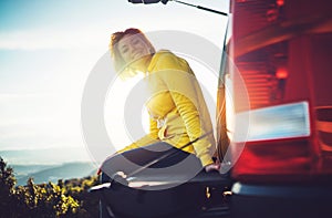 Tourist traveler traveling in car on green top on mountain, young girl smiles happily against background sunset in the mountains h