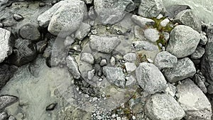 A tourist with trekking poles walks over rocks in a shallow mountain stream.